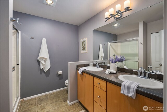 full bathroom with a shower stall, baseboards, double vanity, and toilet