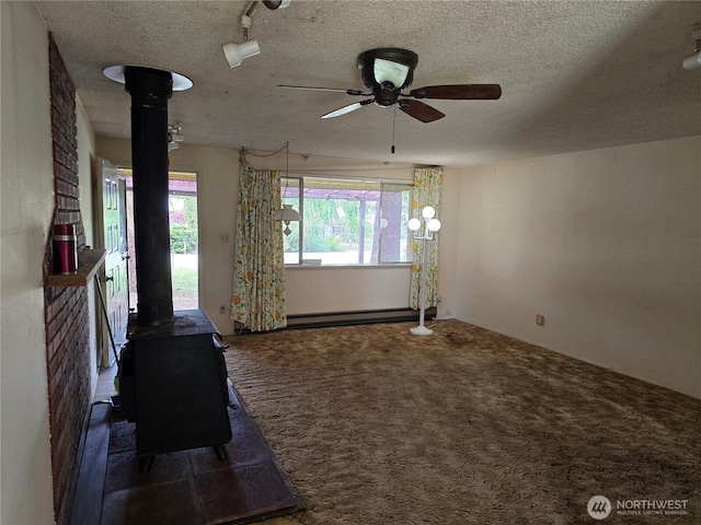 unfurnished living room featuring a wood stove, a ceiling fan, a baseboard heating unit, carpet floors, and a textured ceiling
