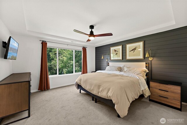 bedroom with a tray ceiling, light colored carpet, baseboards, and a ceiling fan