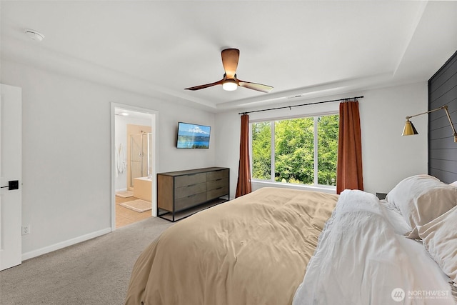 carpeted bedroom with baseboards, a raised ceiling, connected bathroom, and a ceiling fan