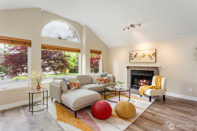 living room with a tile fireplace, wood finished floors, baseboards, rail lighting, and high vaulted ceiling