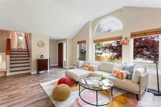 living area featuring healthy amount of natural light, wood finished floors, stairs, baseboards, and high vaulted ceiling
