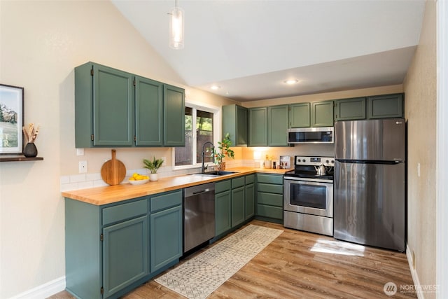 kitchen with appliances with stainless steel finishes, a sink, vaulted ceiling, light wood-style floors, and baseboards