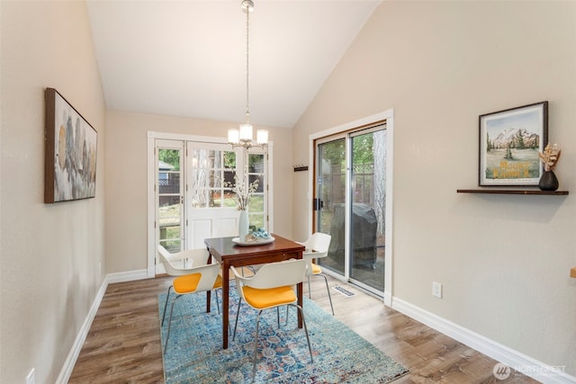 dining space with lofted ceiling, wood finished floors, a chandelier, and baseboards