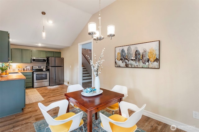 dining area with a chandelier, lofted ceiling, light wood-type flooring, stairs, and baseboards