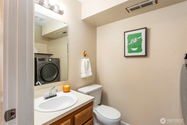 half bath featuring washer / clothes dryer, toilet, vanity, and a textured wall