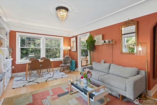 living area featuring wood finished floors, plenty of natural light, baseboards, and ornamental molding