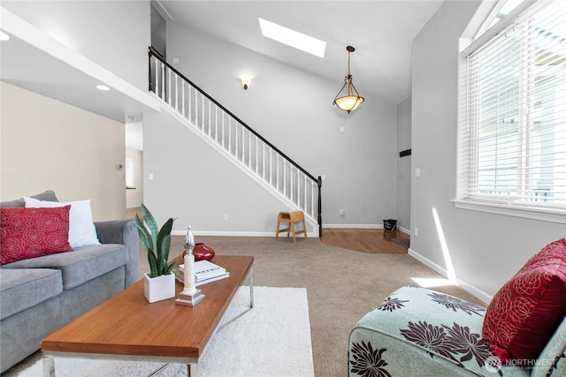 carpeted living room featuring a skylight, stairs, high vaulted ceiling, and baseboards