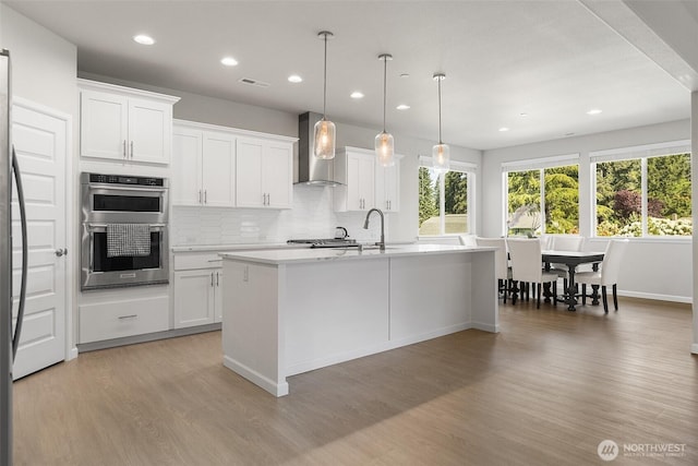 1803 135th Street Ct S, Tacoma, WA 98444 - kitchen featuring wall chimney exhaust hood, stainless steel double oven, light countertops, tasteful backsplash, and light wood-type flooring
