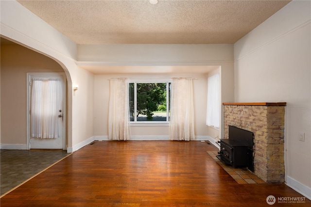 766 120th St S Unit A & B, Tacoma, WA 98444 - unfurnished living room featuring a wood stove, wood finished floors, arched walkways, a textured ceiling, and baseboards