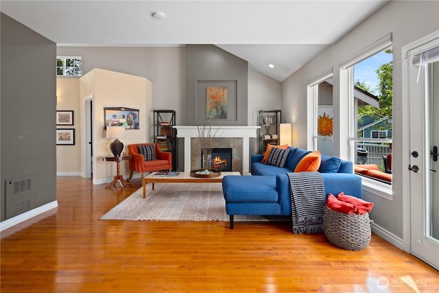 living room featuring lofted ceiling, a fireplace, light wood-type flooring, and baseboards