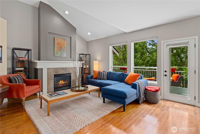 living area featuring plenty of natural light, wood finished floors, a tiled fireplace, lofted ceiling, and recessed lighting