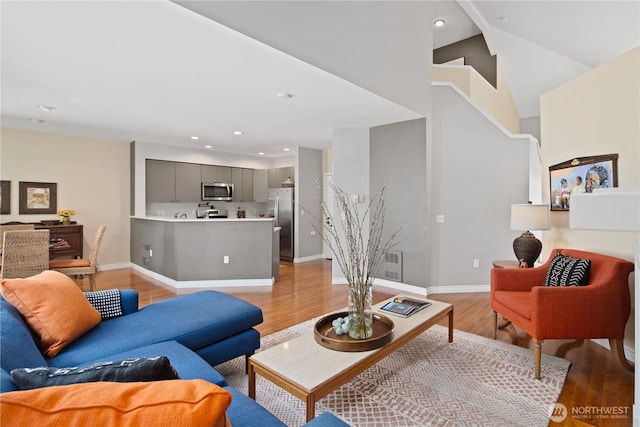 living room with light wood-style floors, baseboards, recessed lighting, and high vaulted ceiling
