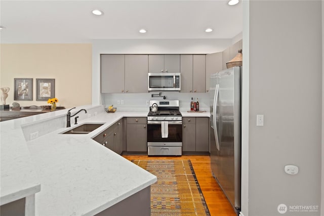 kitchen featuring stainless steel appliances, gray cabinets, a sink, light wood-style flooring, and recessed lighting