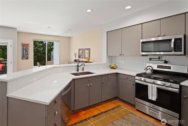 kitchen featuring appliances with stainless steel finishes, a sink, gray cabinets, a peninsula, and light wood-style floors