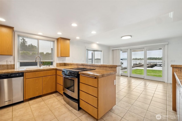 kitchen with appliances with stainless steel finishes, a peninsula, a sink, light tile patterned flooring, and recessed lighting