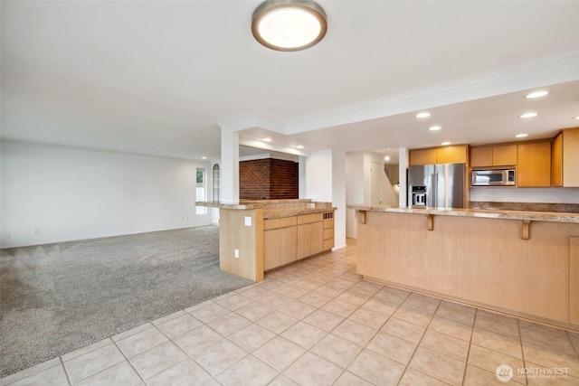 kitchen featuring appliances with stainless steel finishes, a kitchen breakfast bar, open floor plan, light brown cabinetry, and recessed lighting