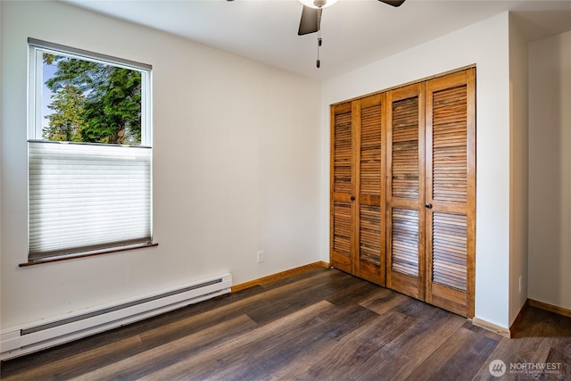 unfurnished bedroom with a baseboard heating unit, dark wood finished floors, a closet, baseboards, and a ceiling fan