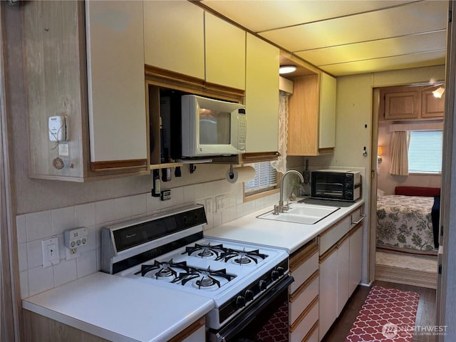 kitchen featuring range with gas stovetop, white microwave, a sink, backsplash, and light countertops