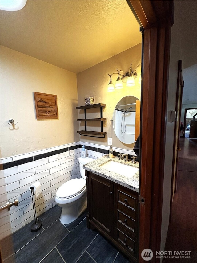 54 Jaquish Rd, Omak, WA 98841 - bathroom featuring wainscoting, tile walls, toilet, vanity, and a textured ceiling