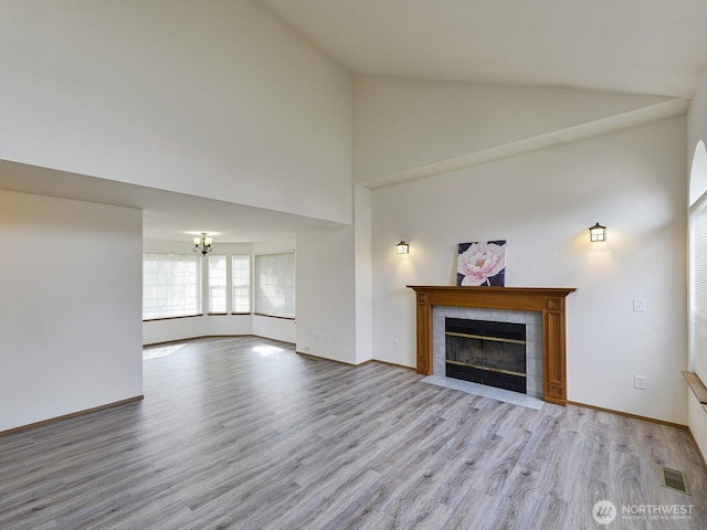 unfurnished living room featuring a fireplace, a chandelier, wood finished floors, high vaulted ceiling, and baseboards