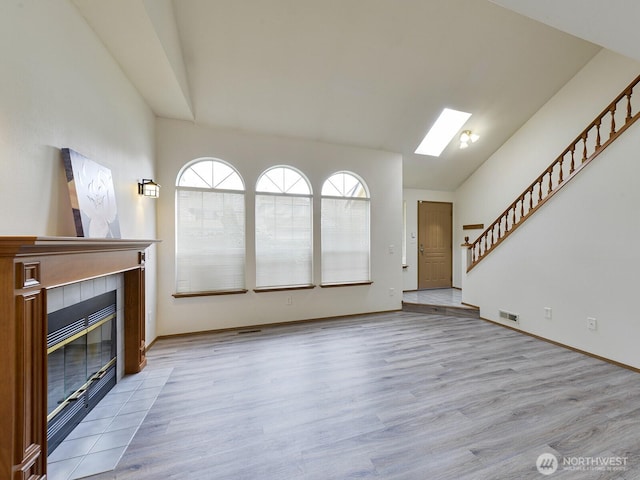unfurnished living room with a fireplace, wood finished floors, stairs, lofted ceiling, and baseboards