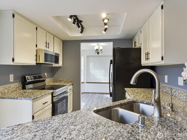 kitchen with appliances with stainless steel finishes, a sink, a tray ceiling, light stone counters, and white cabinets