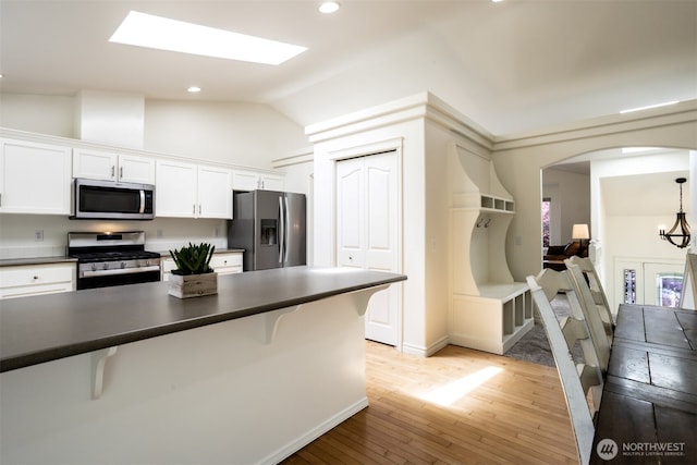 kitchen featuring stainless steel appliances, a breakfast bar, dark countertops, vaulted ceiling, and recessed lighting