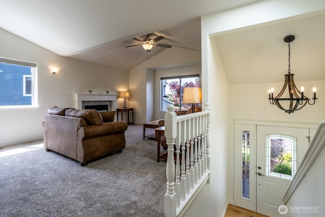 carpeted entrance foyer featuring vaulted ceiling, a chandelier, a fireplace, a ceiling fan, and baseboards