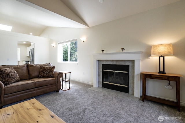 carpeted living area featuring lofted ceiling, a tiled fireplace, arched walkways, and baseboards