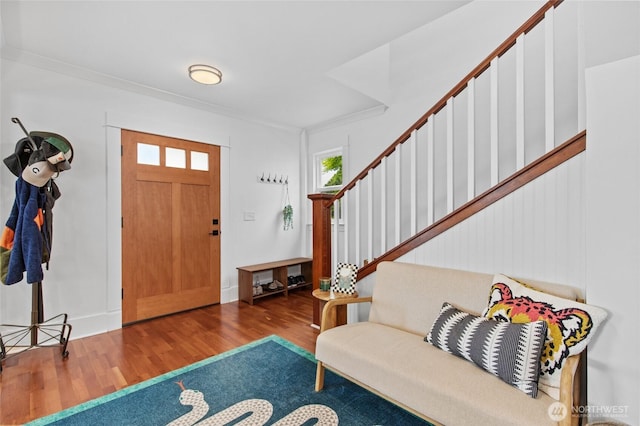 foyer featuring wood finished floors, crown molding, stairs, and baseboards