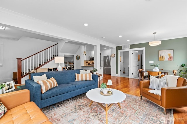 living room featuring wood finished floors, stairway, ornamental molding, and recessed lighting