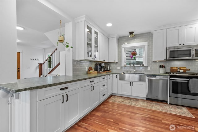 kitchen featuring stainless steel appliances, a sink, a peninsula, light wood finished floors, and recessed lighting