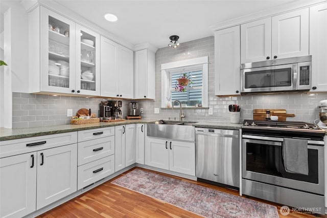 kitchen with appliances with stainless steel finishes, white cabinets, light wood-type flooring, and backsplash