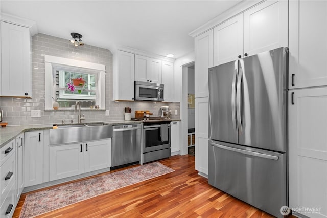 kitchen with stainless steel appliances, a sink, white cabinets, and light wood-style floors