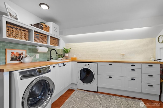 clothes washing area with washing machine and dryer, wood finished floors, and cabinet space