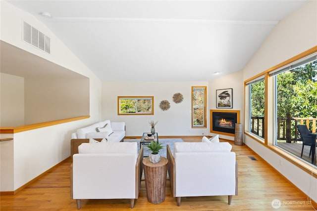 living room with lofted ceiling, a glass covered fireplace, light wood-style flooring, and baseboards