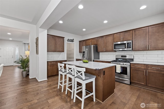 kitchen featuring appliances with stainless steel finishes, backsplash, a kitchen island, dark wood finished floors, and a breakfast bar area