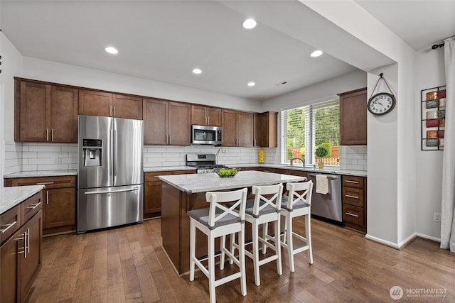 kitchen featuring stainless steel appliances, dark wood finished floors, tasteful backsplash, a kitchen bar, and a center island