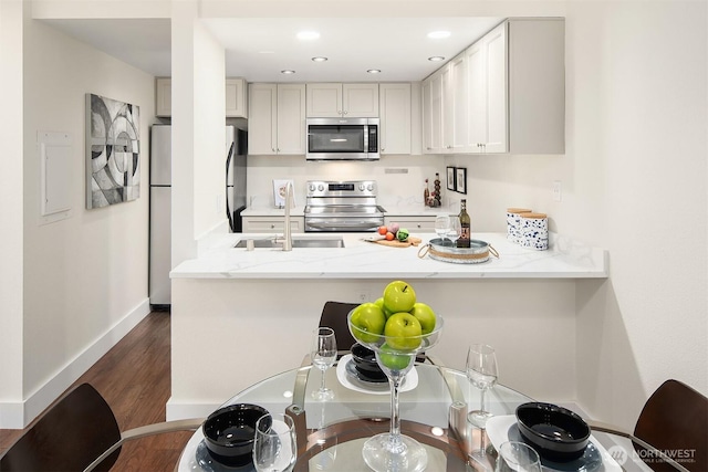 kitchen with stainless steel appliances, a sink, a peninsula, light stone counters, and dark wood finished floors