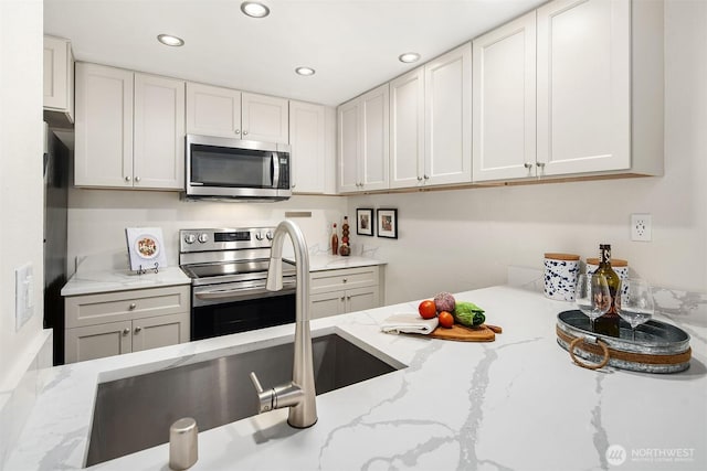 kitchen featuring stainless steel appliances, recessed lighting, white cabinetry, a sink, and light stone countertops