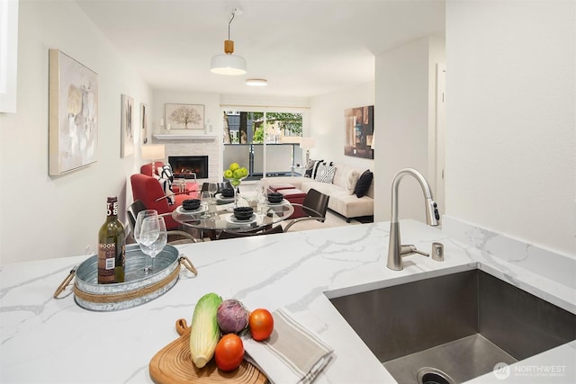 kitchen with a sink, open floor plan, light stone countertops, and a lit fireplace