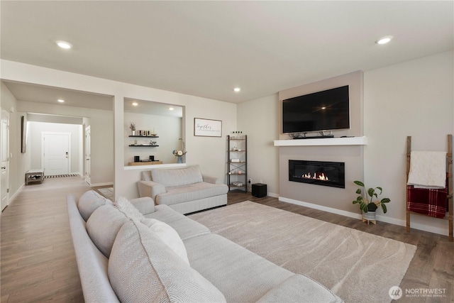 living area featuring wood finished floors, recessed lighting, a glass covered fireplace, and baseboards