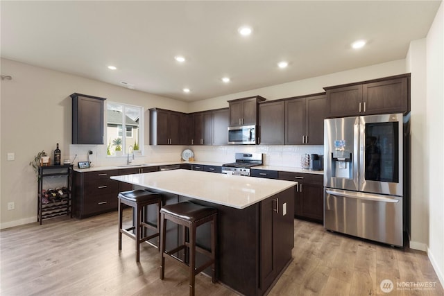 kitchen featuring stainless steel appliances, dark brown cabinets, a kitchen island, light countertops, and a sink