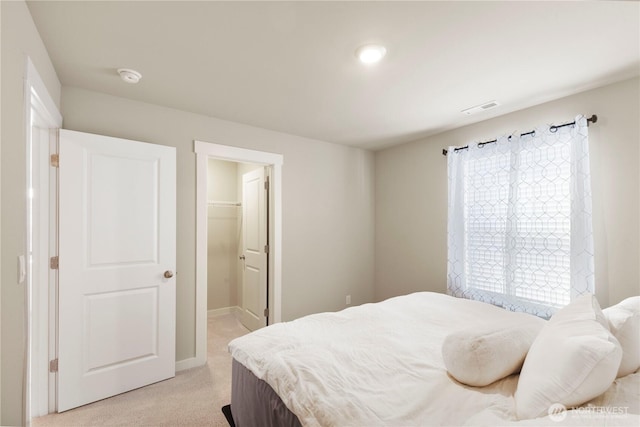 bedroom featuring light colored carpet, a walk in closet, and baseboards