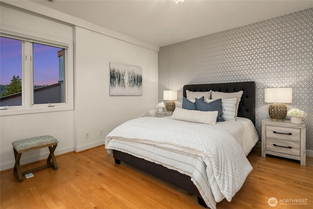 8902 N Mercer Way, Mercer Island, WA 98040 - bedroom featuring an accent wall, wallpapered walls, baseboards, and light wood-style flooring