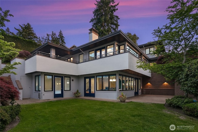 8902 N Mercer Way, Mercer Island, WA 98040 - back of property at dusk featuring a balcony, stucco siding, a lawn, a chimney, and french doors