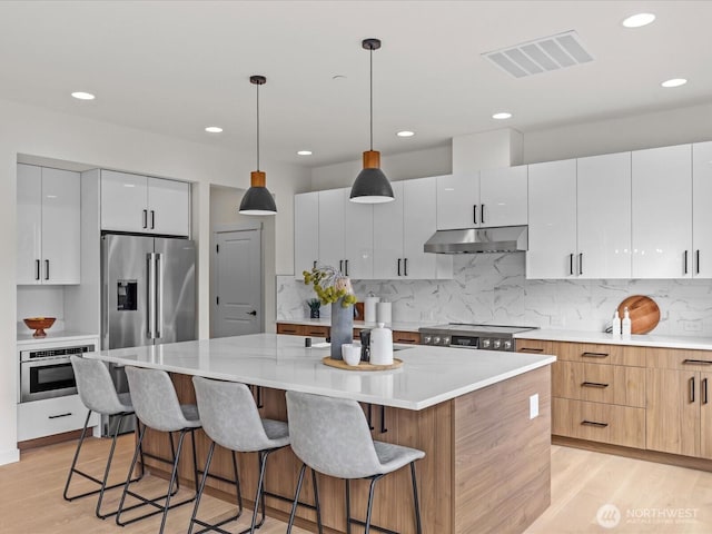 667 17th Ave NW, Issaquah, WA 98027 - kitchen featuring stainless steel appliances, under cabinet range hood, a center island, light wood-type flooring, and recessed lighting