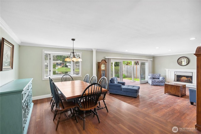 dining room with a chandelier, wood finished floors, crown molding, baseboards, and a lit fireplace