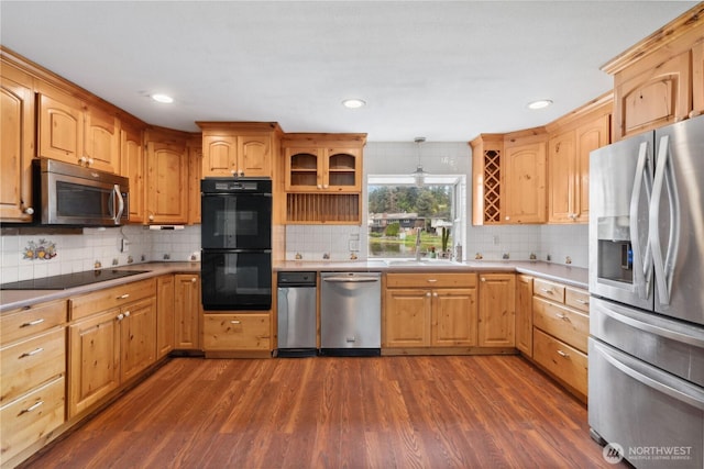 kitchen with black appliances, dark wood-type flooring, backsplash, light countertops, and a sink
